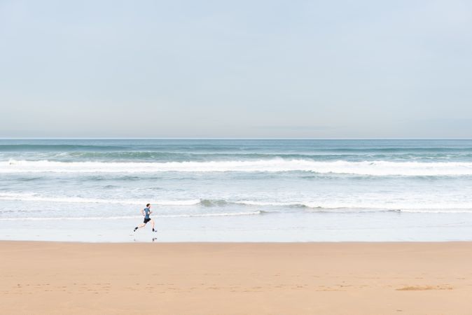 Sportsman in active wear jogging on lonely beach