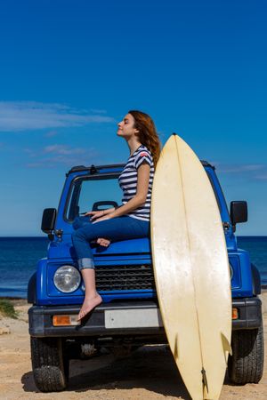 Woman sitting on top of a car with surfboard