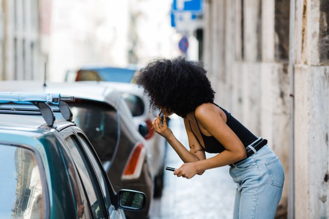 Black female applying lipstick outdoors