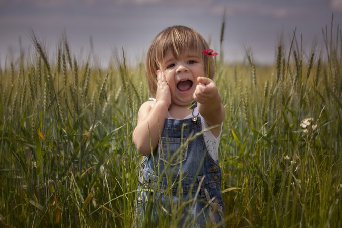 Girl in overhaul holding red flower and smiling in green field