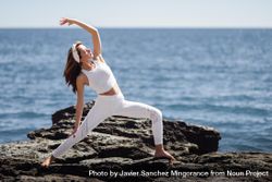 Woman wearing light sport clothes and doing warrior A pose on rocks on the coast 4d21L0
