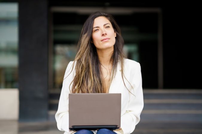 A thoughtful woman is diligently working on her laptop while savoring the stunning outdoors