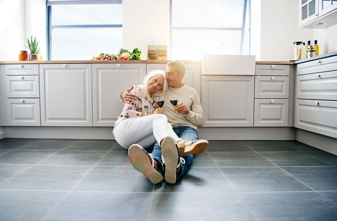 Older couple holding each other on the kitchen floor drinking red wine