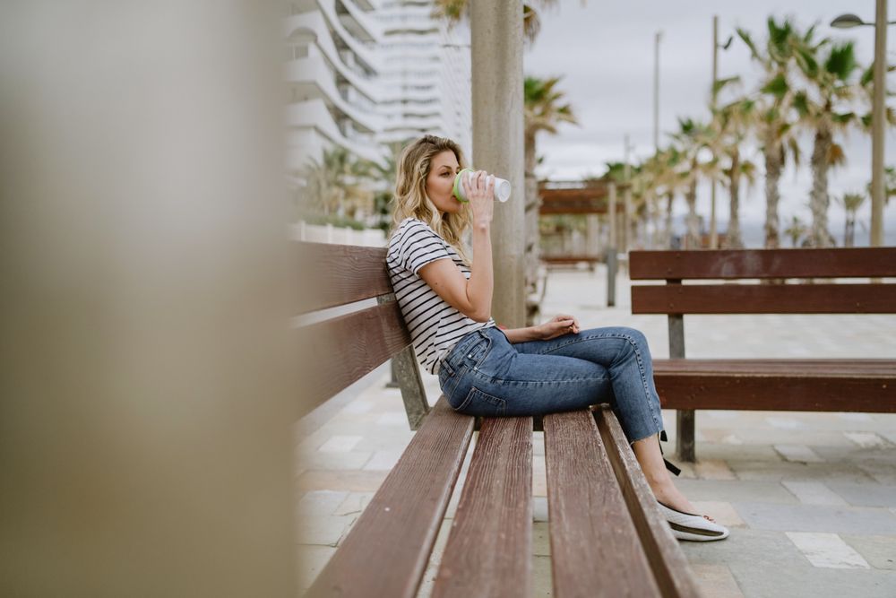 Happy woman with disposable cup of coffee sitting on street bench