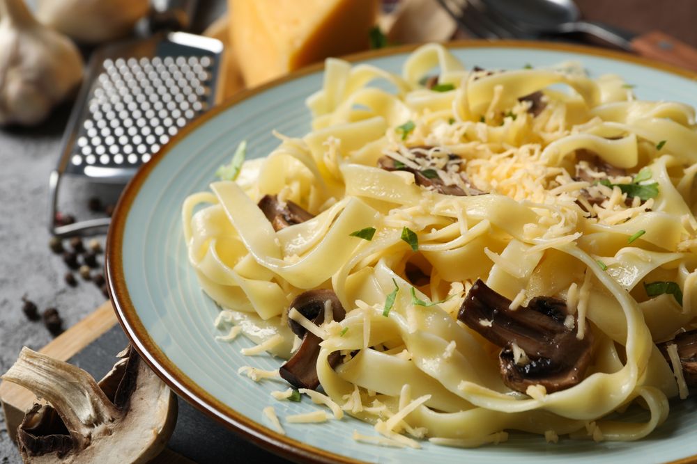 Composition with plate of tasty pasta and ingredients for cooking on gray background