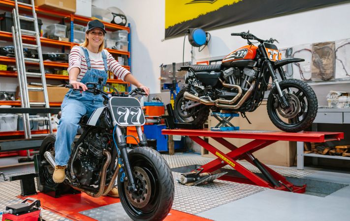 Mechanic woman sitting over motorcycle on factory