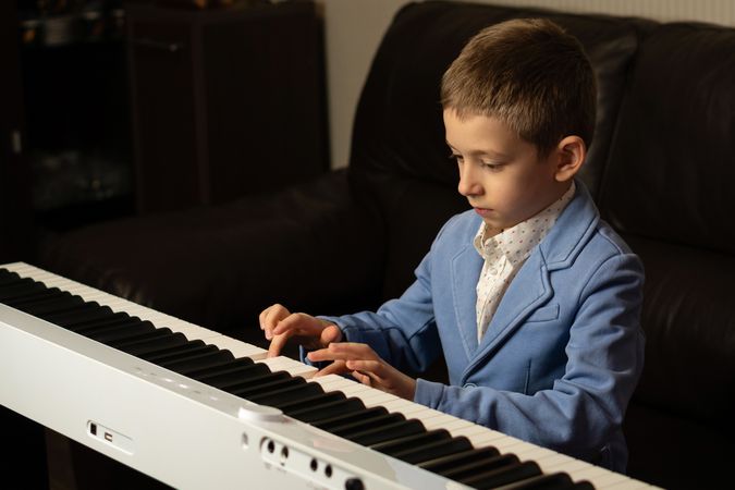Young boy in blue blazer concentrating while playing piano.