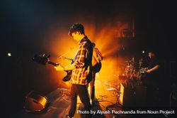 Young white male rock musician  wearing flannel playing bass guitar on stage with orange spotlight 4mW8B0