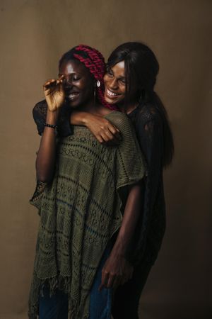 Two African women hugging and laughing against brown wall