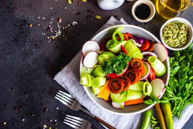 Healthy raw salad with freshly chopped vegetables served with forks and garnishes