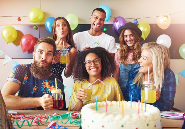 People smiling and making silly faces for the camera at a birthday party with cake and balloons