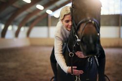 Female horse trainer hugging her horse companion while riding on his back