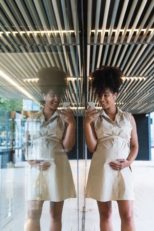 Smiling Black pregnant woman using smartphone and wireless earphones