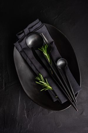 Sleek table setting in dark color with rosemary sprig
