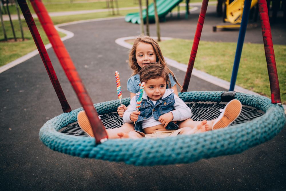 Two kids playing on a swing at a playground