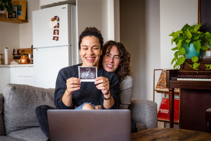 Happy female couple smiling with sonogram picture on video chat announcing their pregnancy