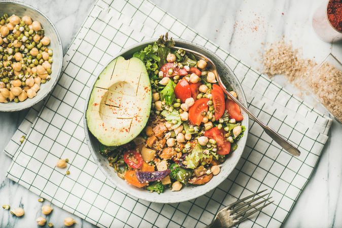 Healthy vegan lunch bowl with avocado, grains, vegetables, on checkered napkin