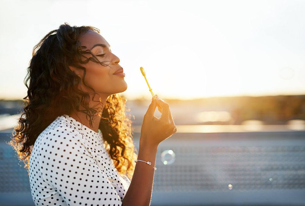 Woman pursing her lips to blow bubbles on sunny rooftop