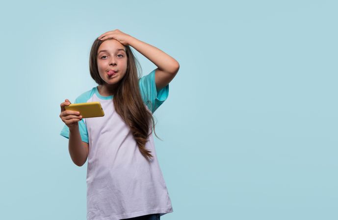 Girl playfully making silly face while using smartphone.