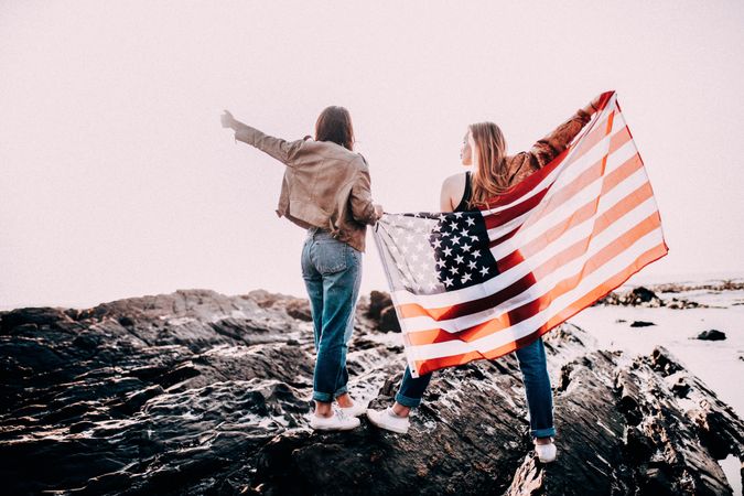 Two young women holding the American flag outside standing atop rocks
