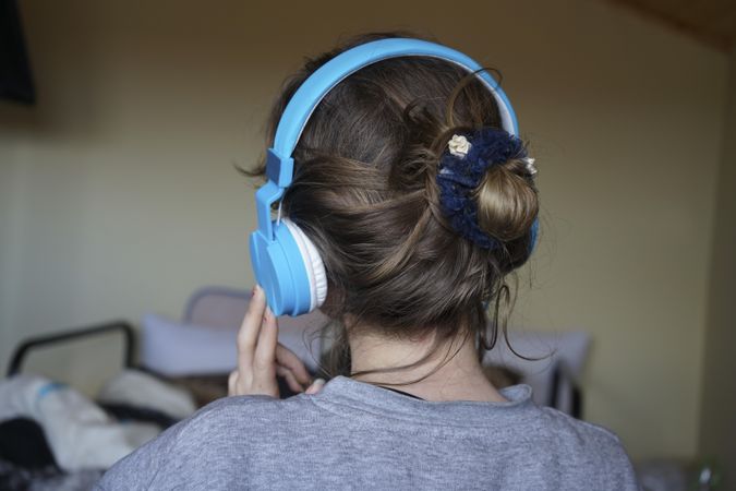 Back view of young woman listening to audio using headphone