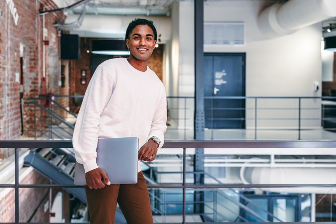 Happy young businessman smiling in a modern office leaning against railings in modern office
