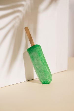 Green ice pop leaning on beige wall with palm tree shadow