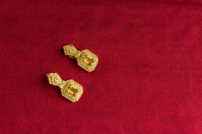 Beautiful shiny golden earrings with diamond studded Indian traditional design on a red velvet background