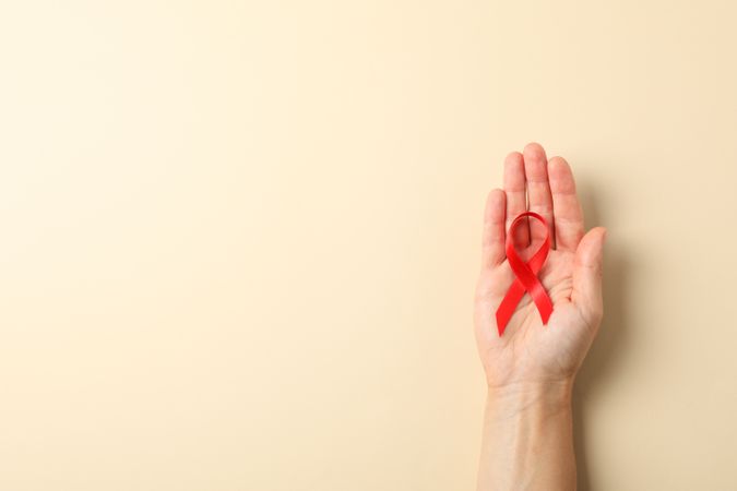 Female hand hold red awareness ribbon on color background, space for text