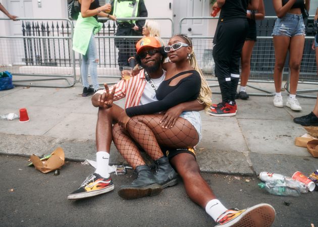 London, England, United Kingdom - August 28, 2022: Happy Black couple sitting on curb at Carnival