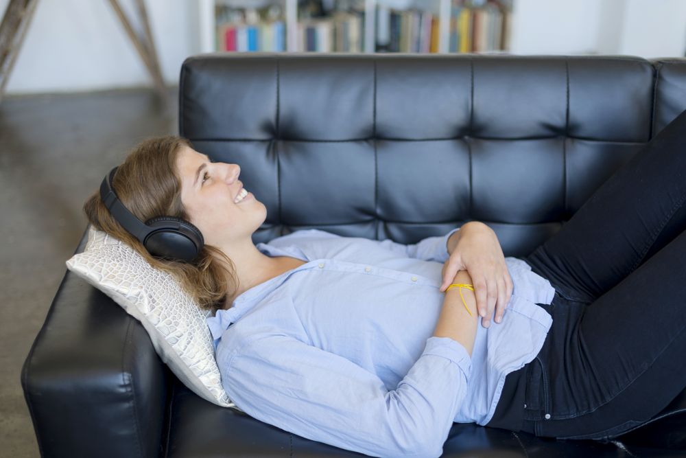Smiling brunette relaxing on the couch and listening music in the living room