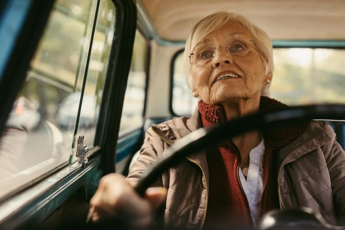Portrait of a woman with gray hair and glasses in winter clothes driving a car