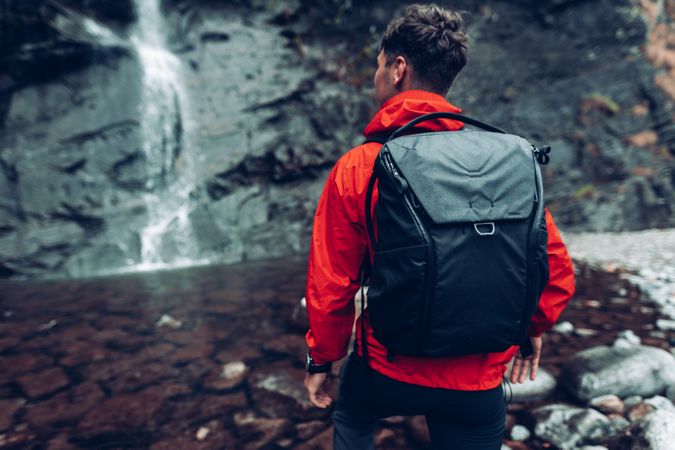 Back view of a man in red jacket with backpack standing against waterfalls
