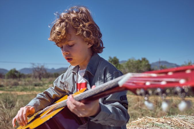 Little boy playing acoustic guitar on sunny day in countryside