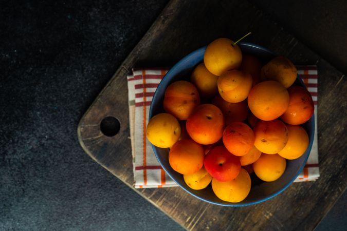 Top view of bowl of orange plums on wooden counter