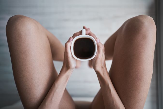 Faceless woman with coffee sitting in room at home