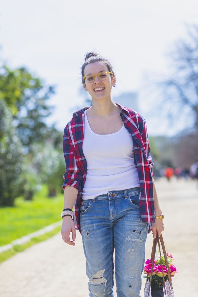 Front view of a young smiling hipster woman walking in a park in sunny day while holding a wicked basket
