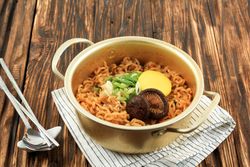 Brass pot full of noodles with radish, onion and mushroom garnish
