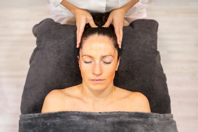 Young woman with cosmetic mask on face lying in beauty center
