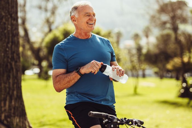Mature man in fitness wear drinking water sitting on his bicycle
