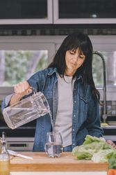 Woman pouring water in her kitchen. Vertical shot