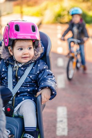 Portrait of observant girl with pink helmet on in bike seat enjoying ride, vertical
