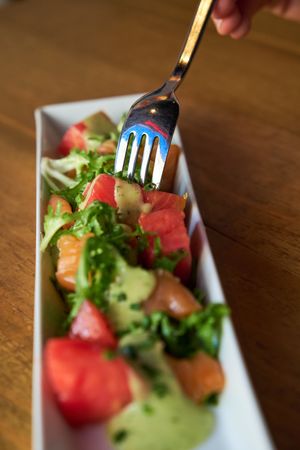 Hand of a man eating with a fork a marinated salmon salad