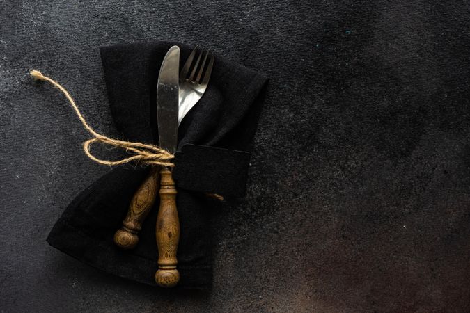Top view of dark silverware in matching napkin on counter with copy space