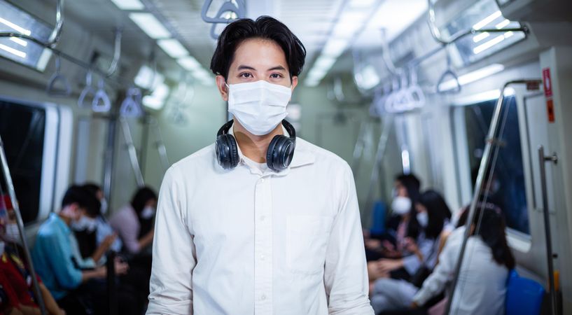 Portrait of man in facemask and headphones standing in metro car