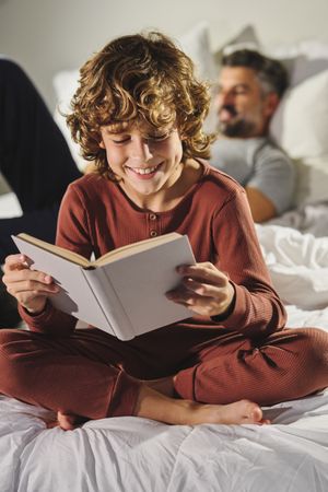 Child reading book on bed against father