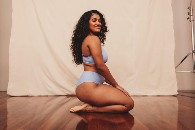 Smiling young woman kneeling in blue underwear against a studio background