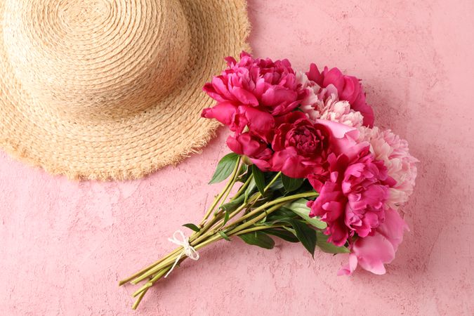 Bouquet of beautiful peonies and straw hat on color background, space for text