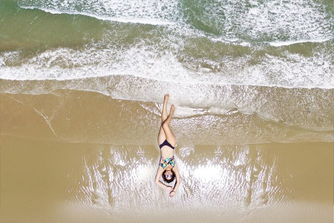 High angle view of woman in a bikini laying on beach shore