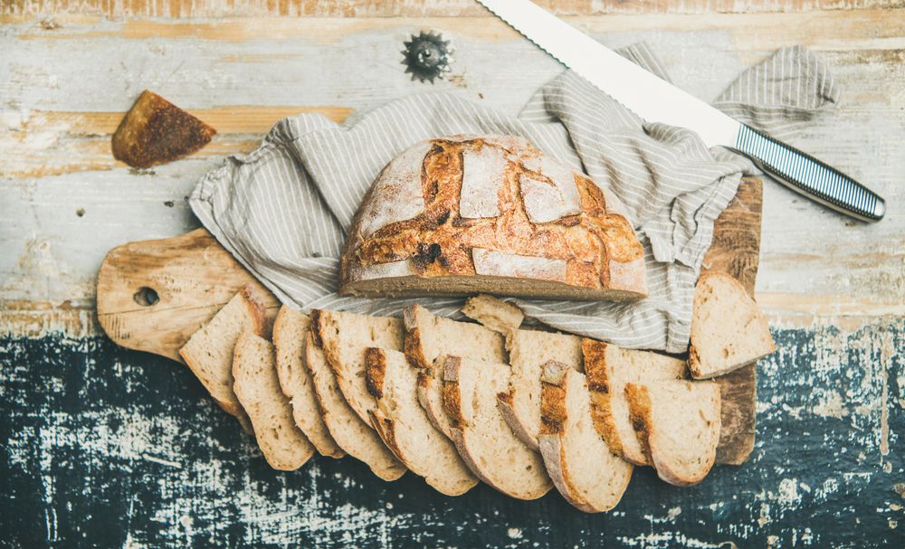 Homemade loaf with slices arranged in line with serrated knife, on wooden board